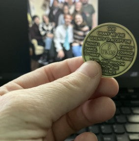 Hand holding a bronze recovery coin with text against a blurred background  of my family 