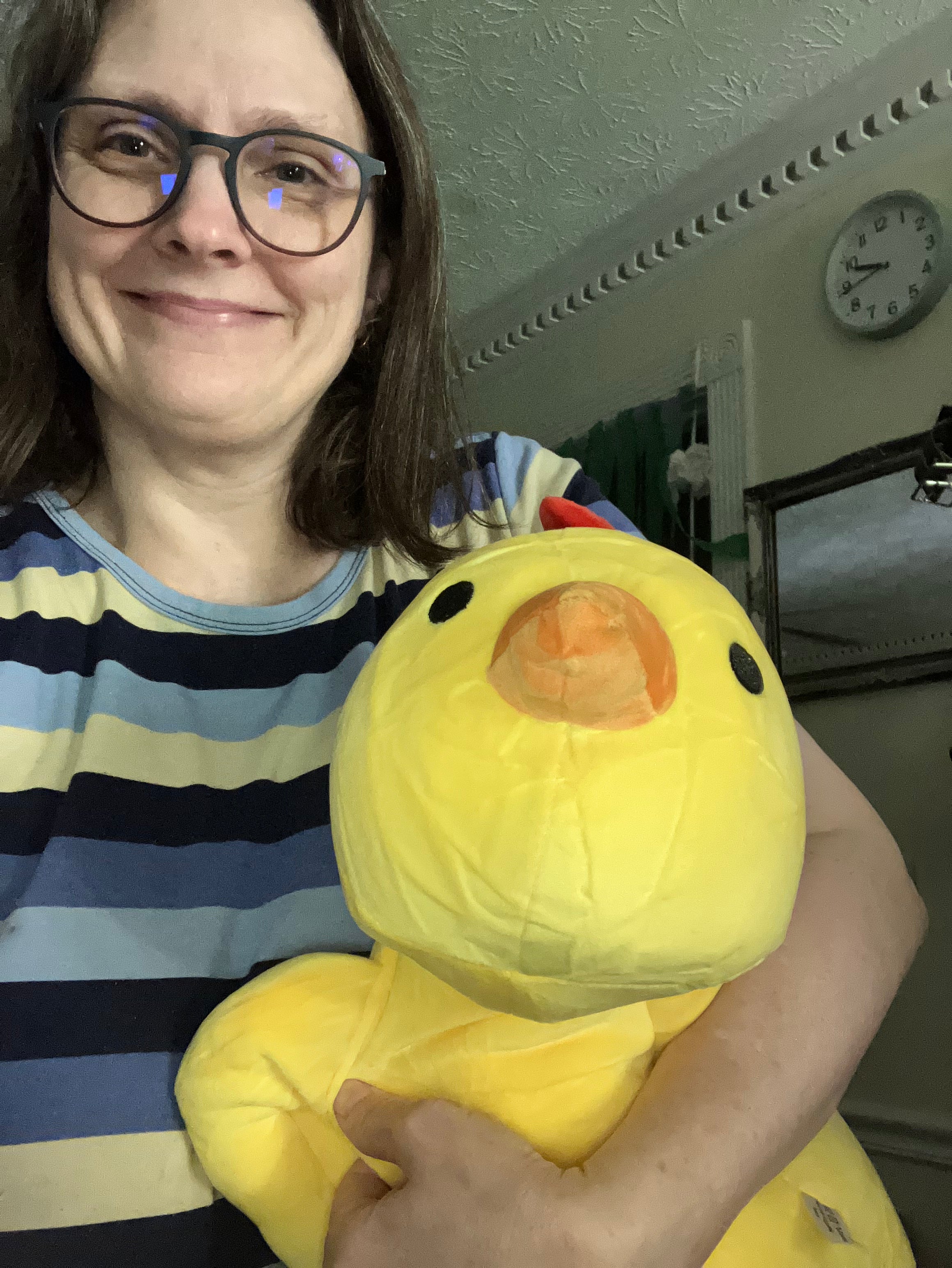 Kelley M Likes holding a large yellow plush chicken toy indoors.