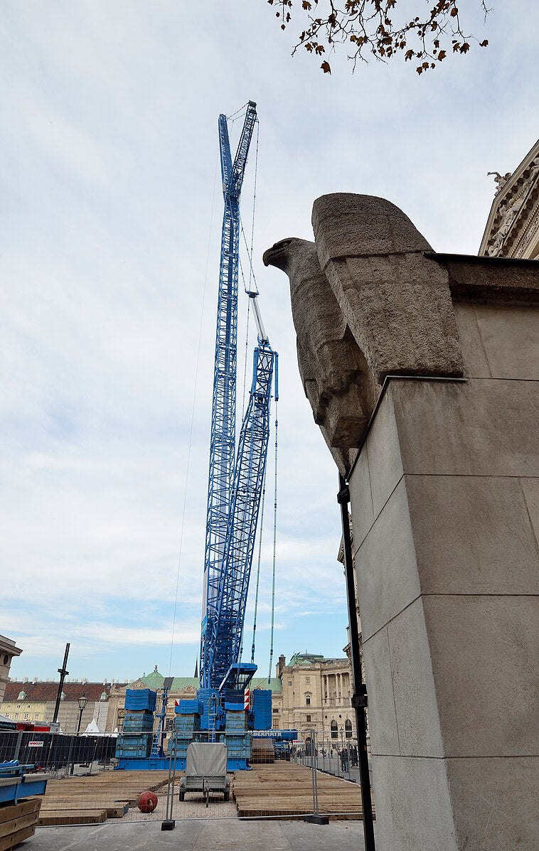 Construction crane next to a large stone sculpture or architectural element against a cloudy sky.