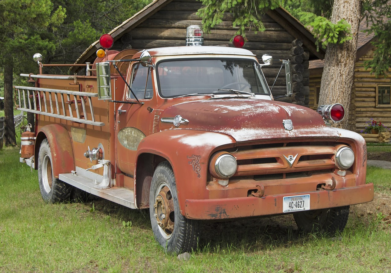 Rustic old fire truck in a grassy area with a log cabin in the background